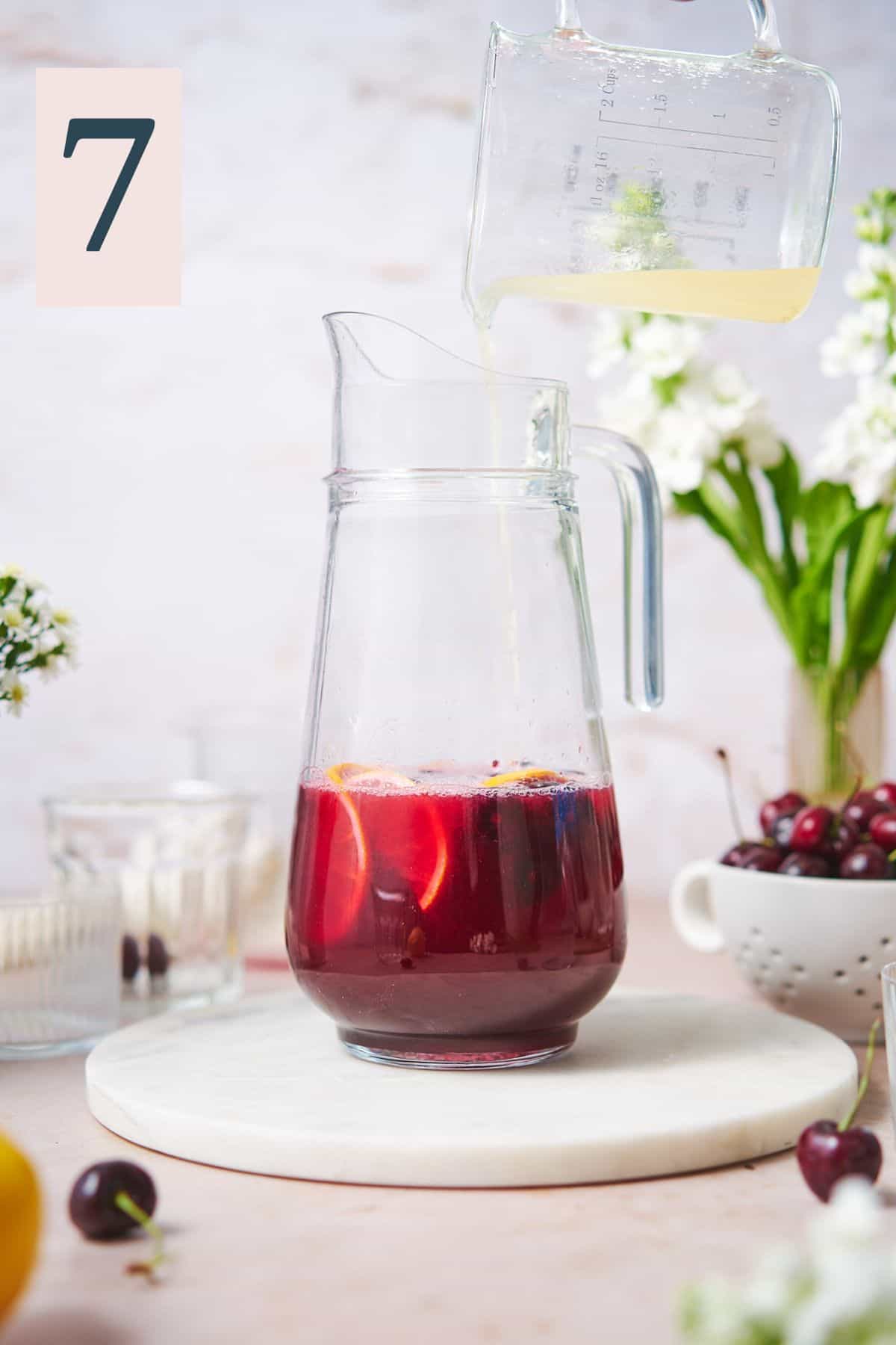 hand pouring lemon juice into a pitcher with cherry simple syrup. 