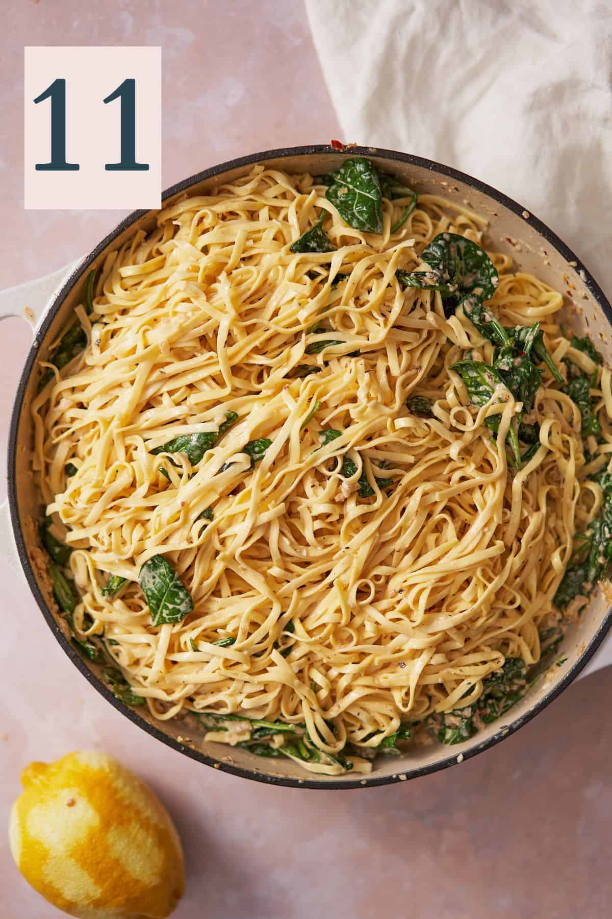 noodles added to a creamy cheese sauce with spinach in an enameled cast iron skillet. 