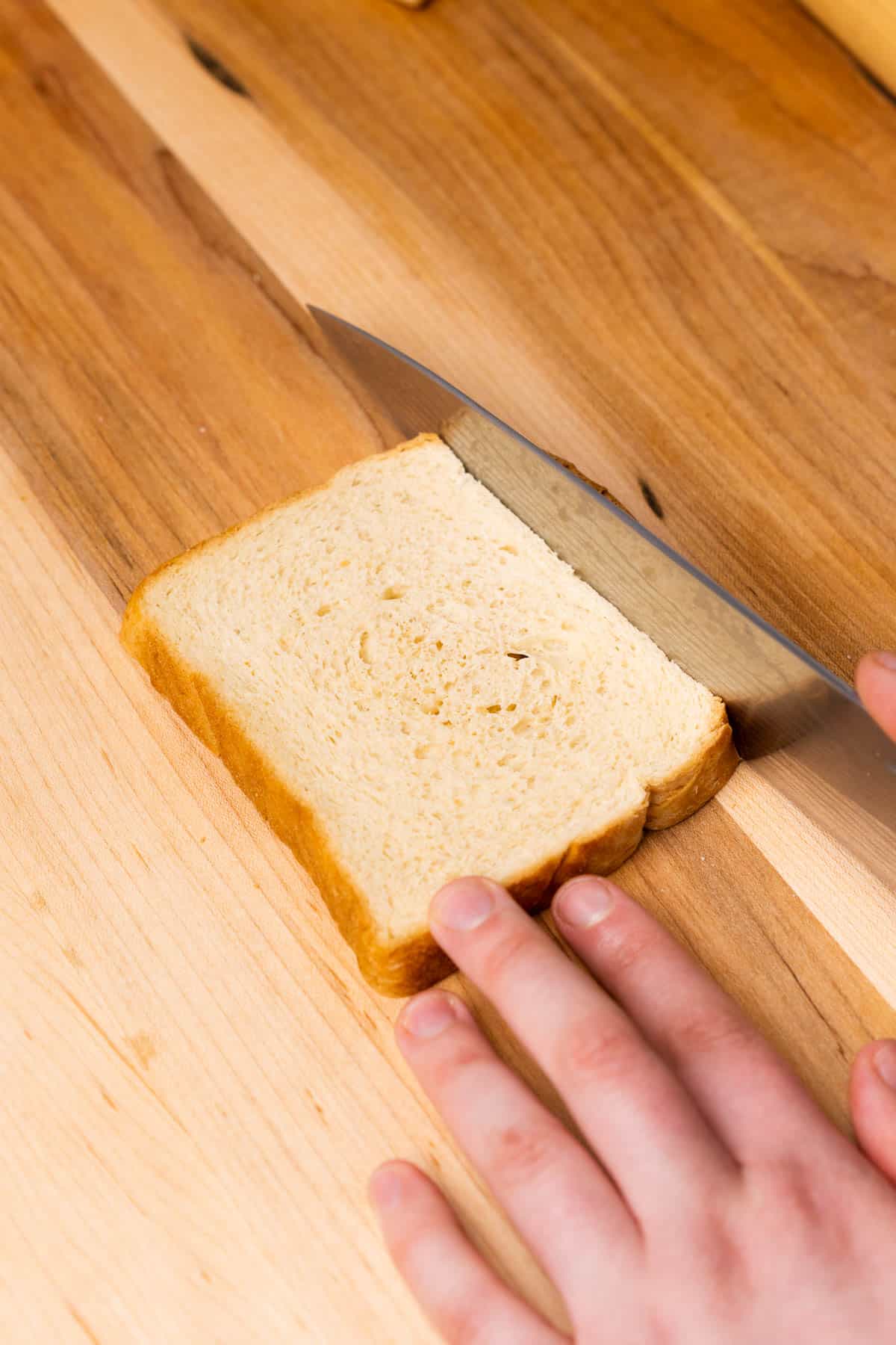 hand cutting crust off of bread on a wood cutting board