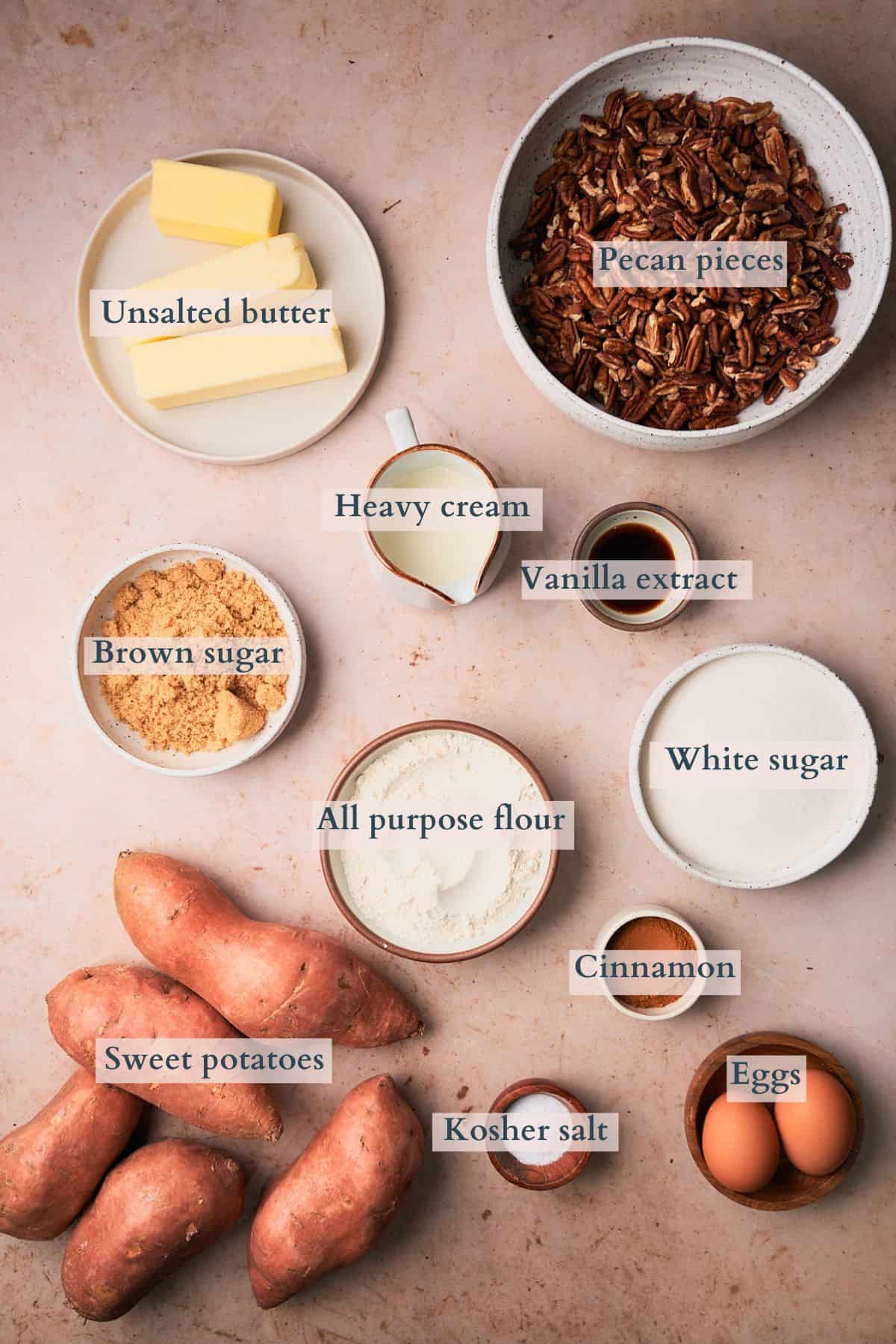 Ingredients to make an old fashioned sweet potato casserole laid out on a table in small bowls and labeled to denote each ingredient. 