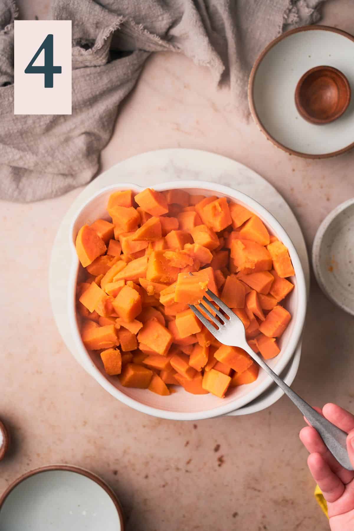 sweet potato pieces steaming hot in a mixing bowl, with a fork stuck into a piece of potato. 