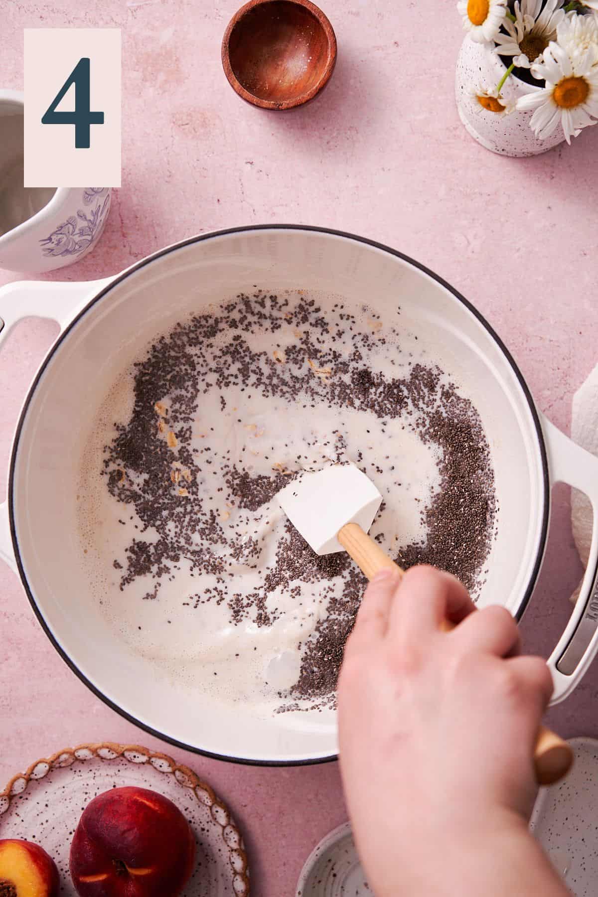 hand stirring chia seeds into a pot with milk and oats. 